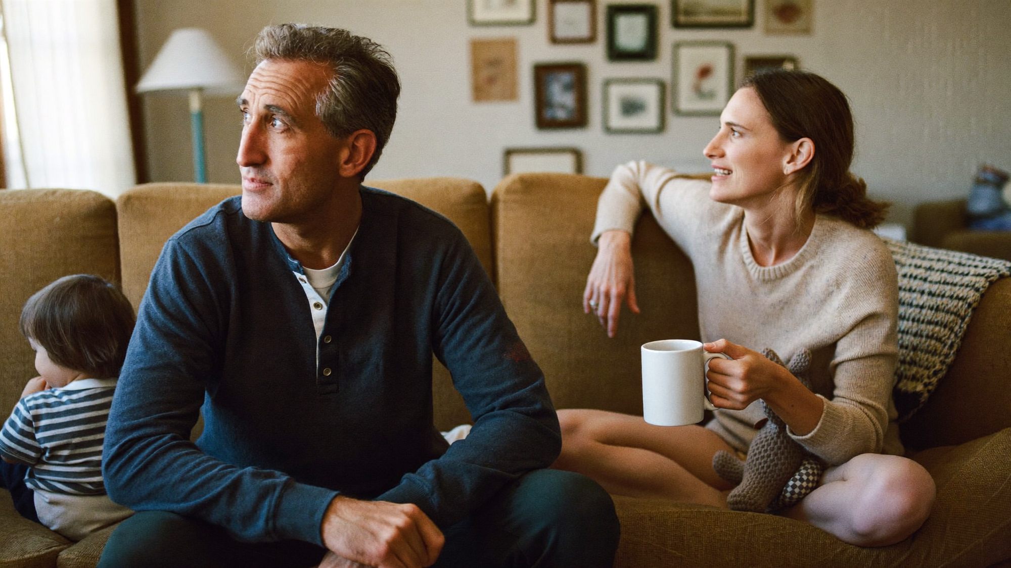 A father in his fifties talks with his adult daughter in a middle Georgia living room while a grandchild plays nearby, illustrating how per stirpes passes an inheritance down a family branch